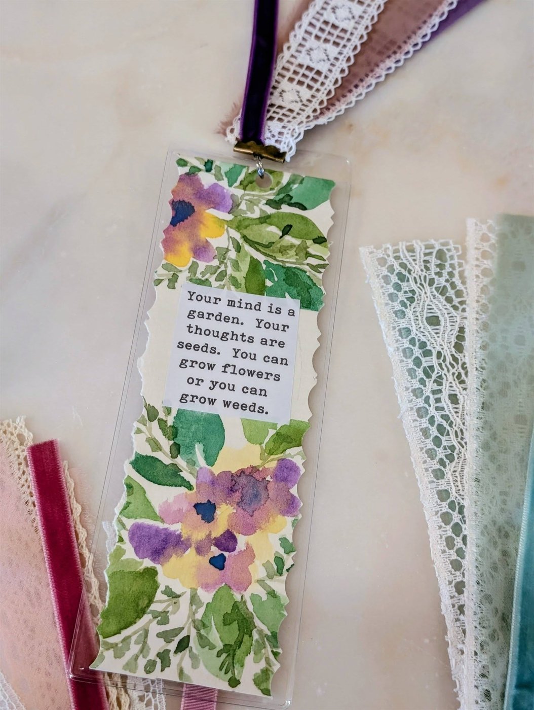 A handmade floral watercolor bookmark finished with velvet and lace ribbon